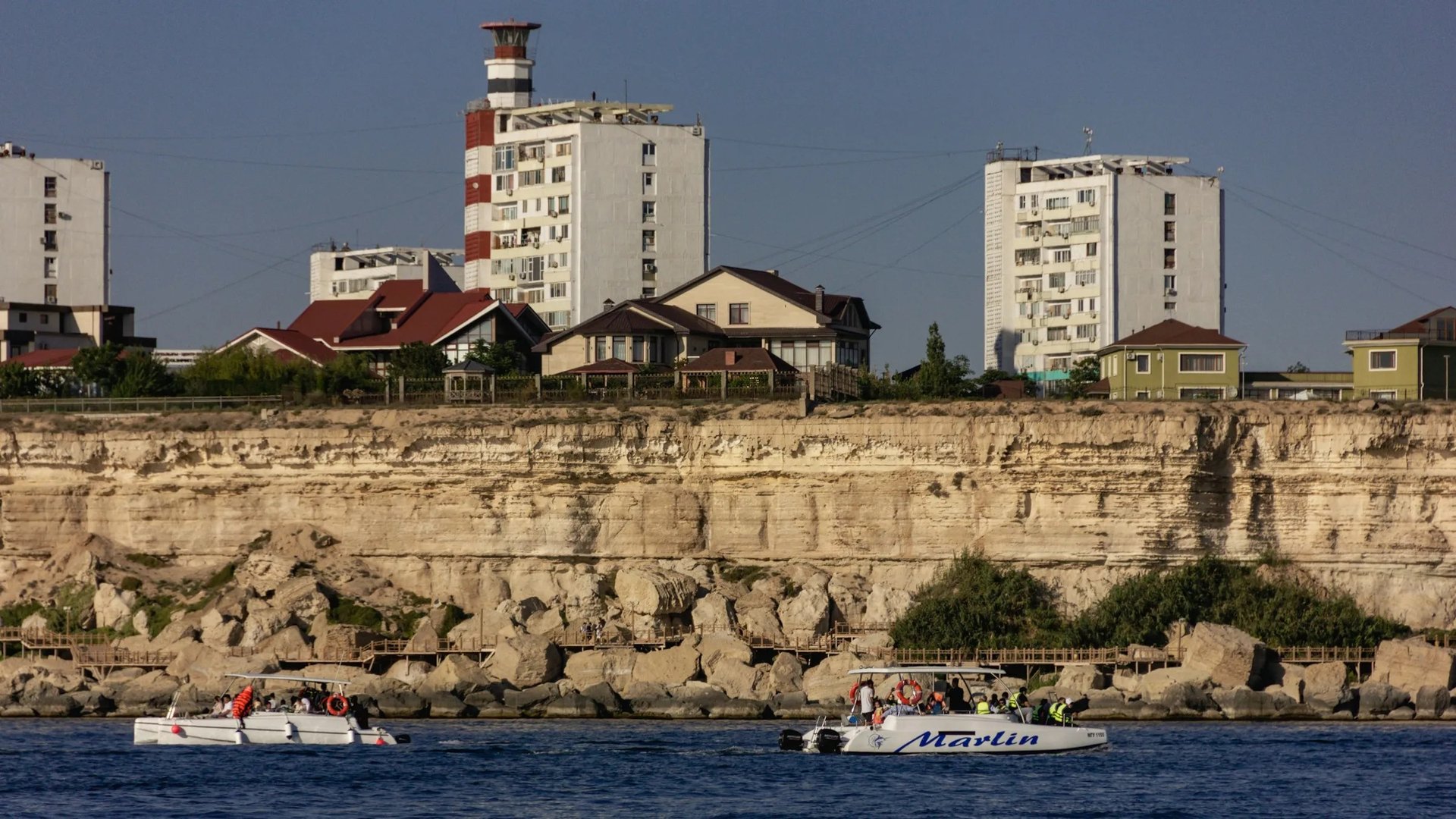 Скалистый берег Каспийского моря в Актау — слоистые жёлтые обрывы, бирюзовые волны и набережная с фонарями