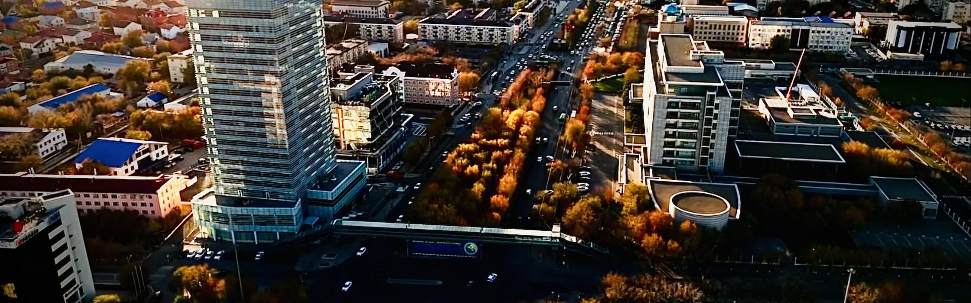 Атырау сверху осенью — высотка офисного центра, деревья в золотой листве и широкая улица в часы заката