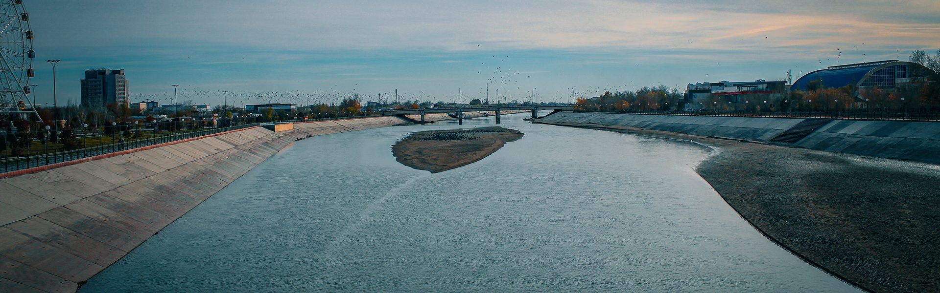 Канал Дослик в Нукусе вечером — мост, колесо обозрения и жилые кварталы вдоль бетонной набережной